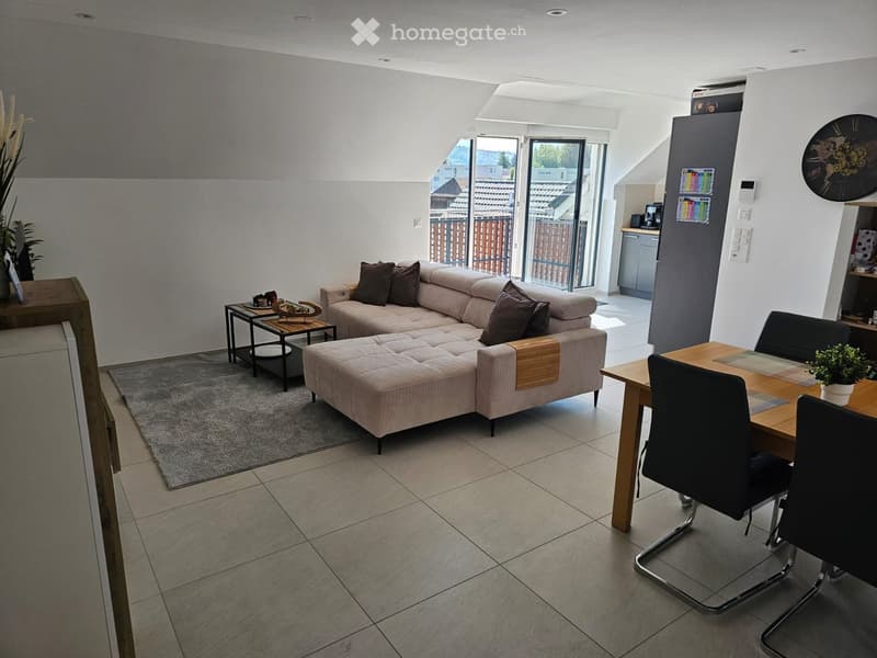 Bright living and dining area with a grey sectional sofa, coffee table, dining table with chairs, and decorative plants.