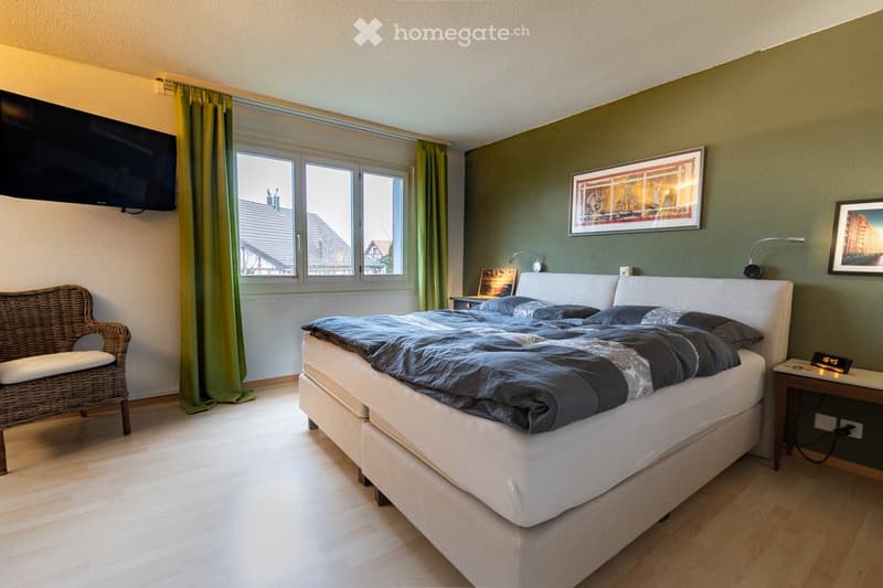 Bedroom. Cozy bedroom with a large bed, wicker chair, nightstand, wall-mounted TV, and picture frames on the walls.