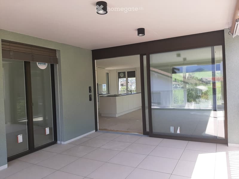 Hallway with large sliding glass doors leading to a modern kitchen and outdoor area, white tiled floor, recessed lighting, and a view of the landscape beyond.