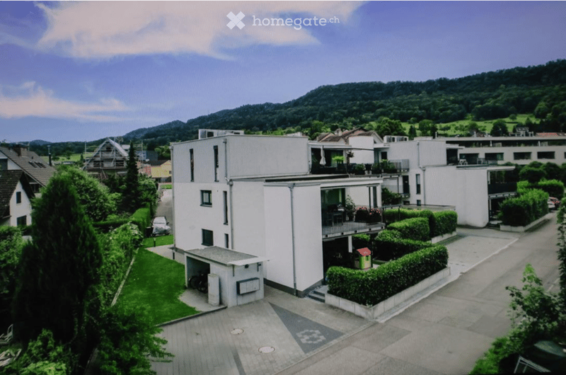 Modern multi-story residential building with white exterior, balconies, garage, and parking area.
