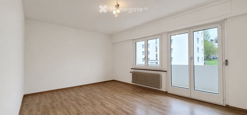 Empty room with wooden flooring, white walls, large windows, and a radiator. No furniture or equipment present.