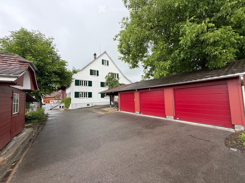 A two-story white house with green shutters and a red garage with three large doors.