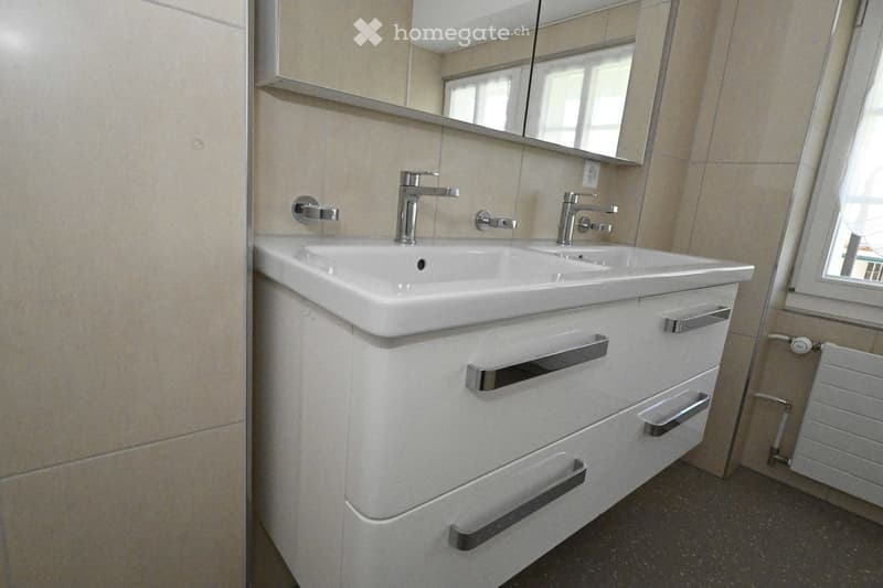 Modern bathroom with a double sink, sleek chrome faucets, a large mirror, and a white cabinet with multiple drawers and handles.