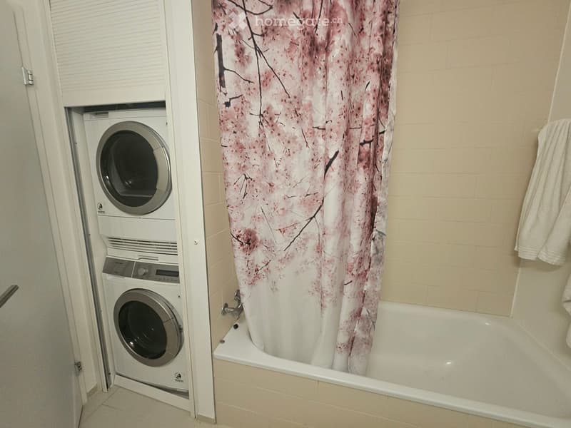 Bathroom with a bathtub, floral shower curtain, and stacked washer/dryer unit.
