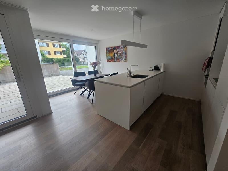 Modern kitchen with light-colored cabinets, a central island, and a dining area. Features a sink, faucet, and a vase on the island.