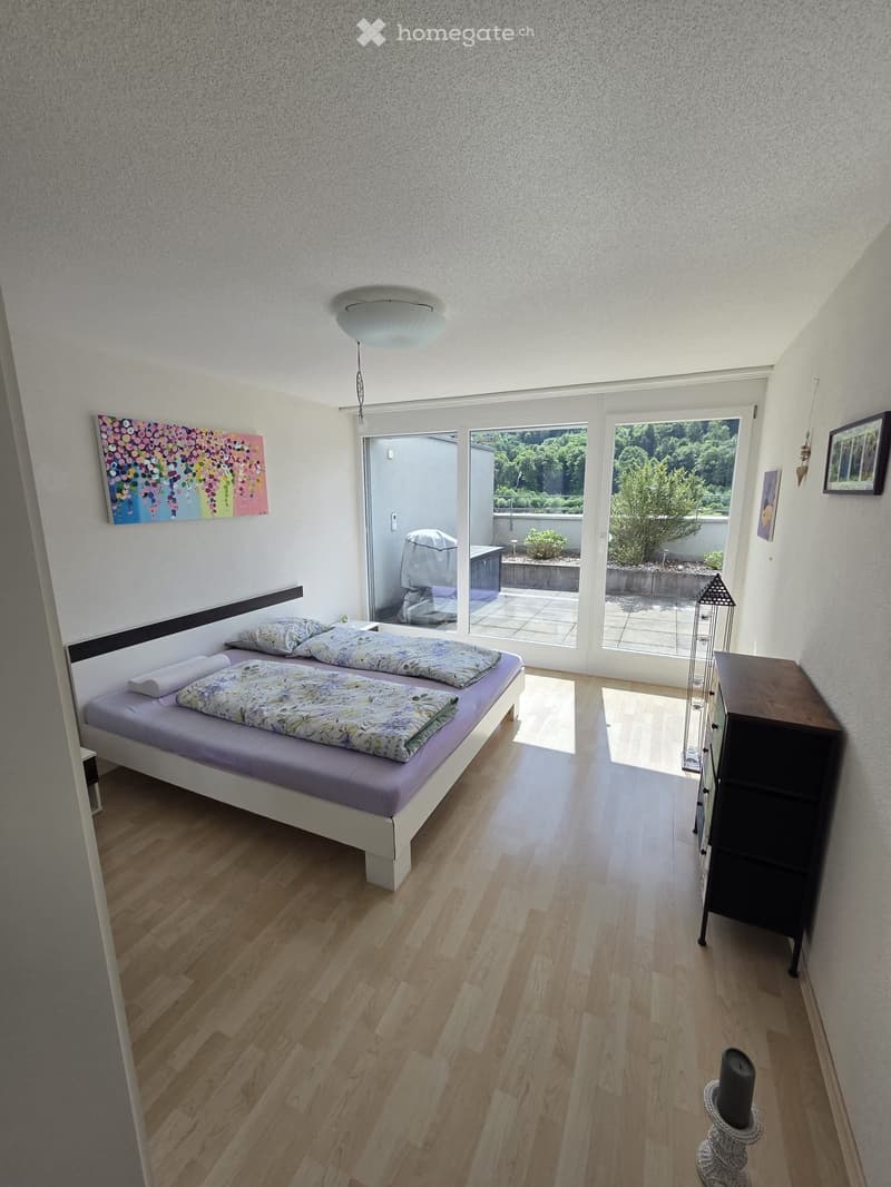 A modern bedroom with a single bed, nightstand, and a view of a small outdoor area through large windows.