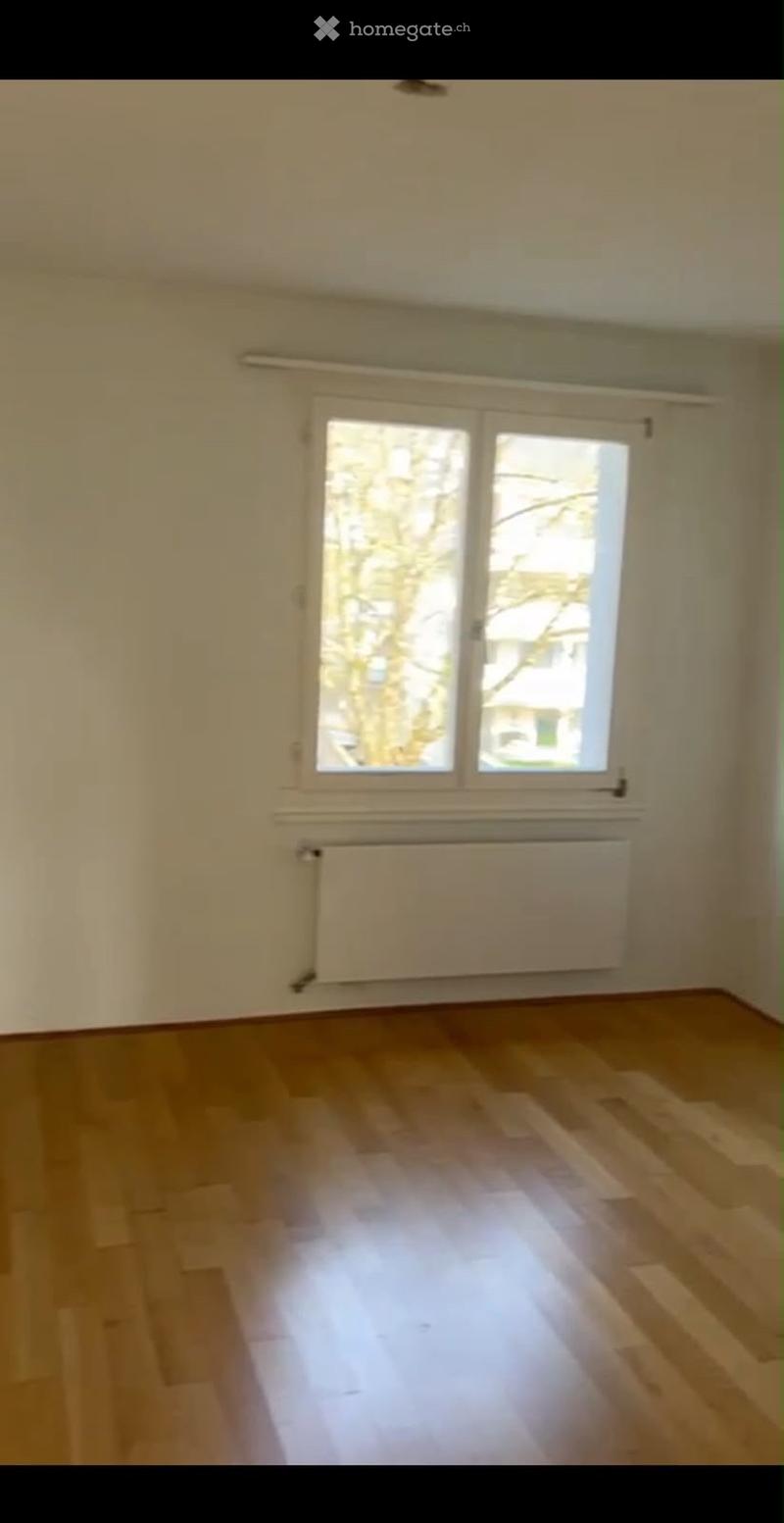 Empty room with wooden flooring, white walls, large window, and radiator under the window.