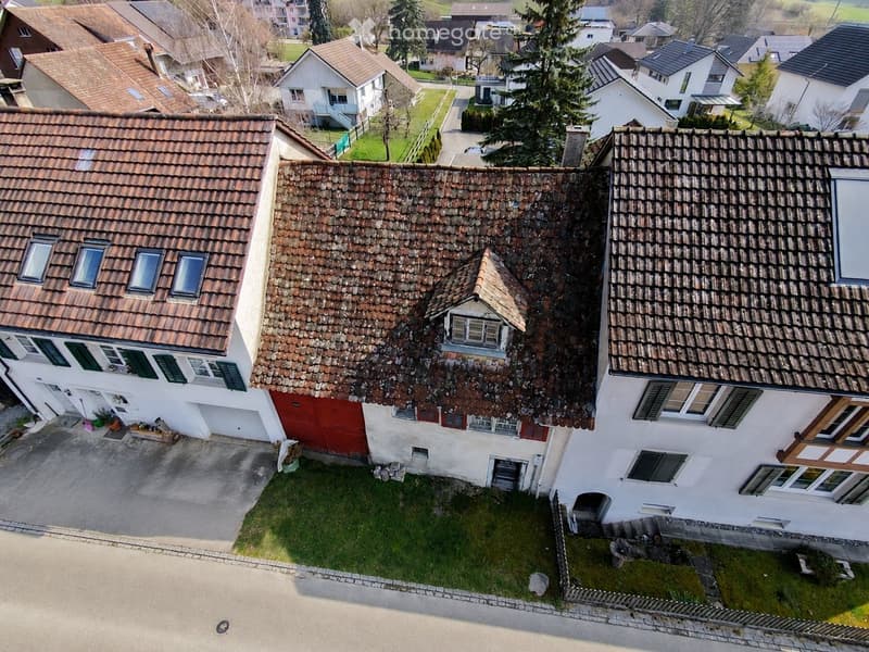 Aerial view of a residential house with a tiled roof, multiple windows, and a small garden area.