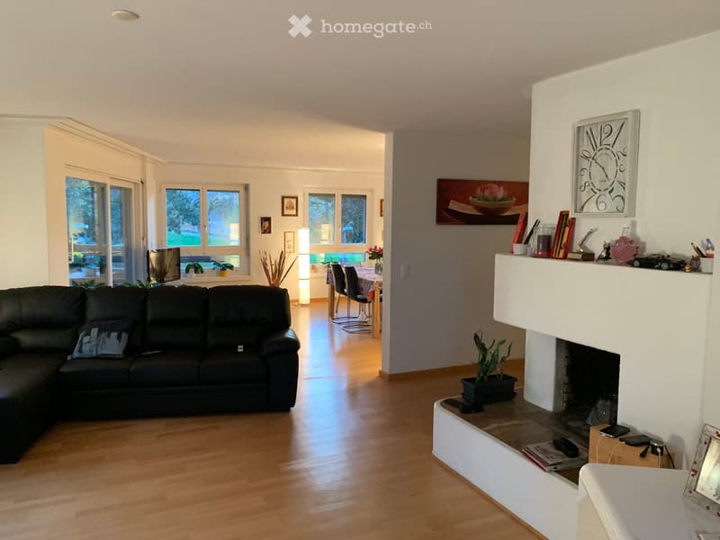 Modern living room with a black sectional sofa, fireplace, dining area with table and chairs, large windows, and decorative items on the mantel.