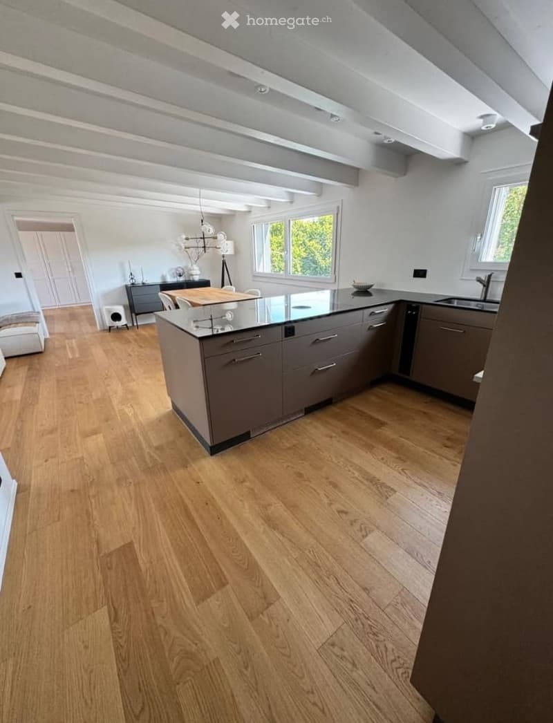 Modern kitchen with light wooden flooring, grey cabinets, a central island, and a dining area with a table and chairs.