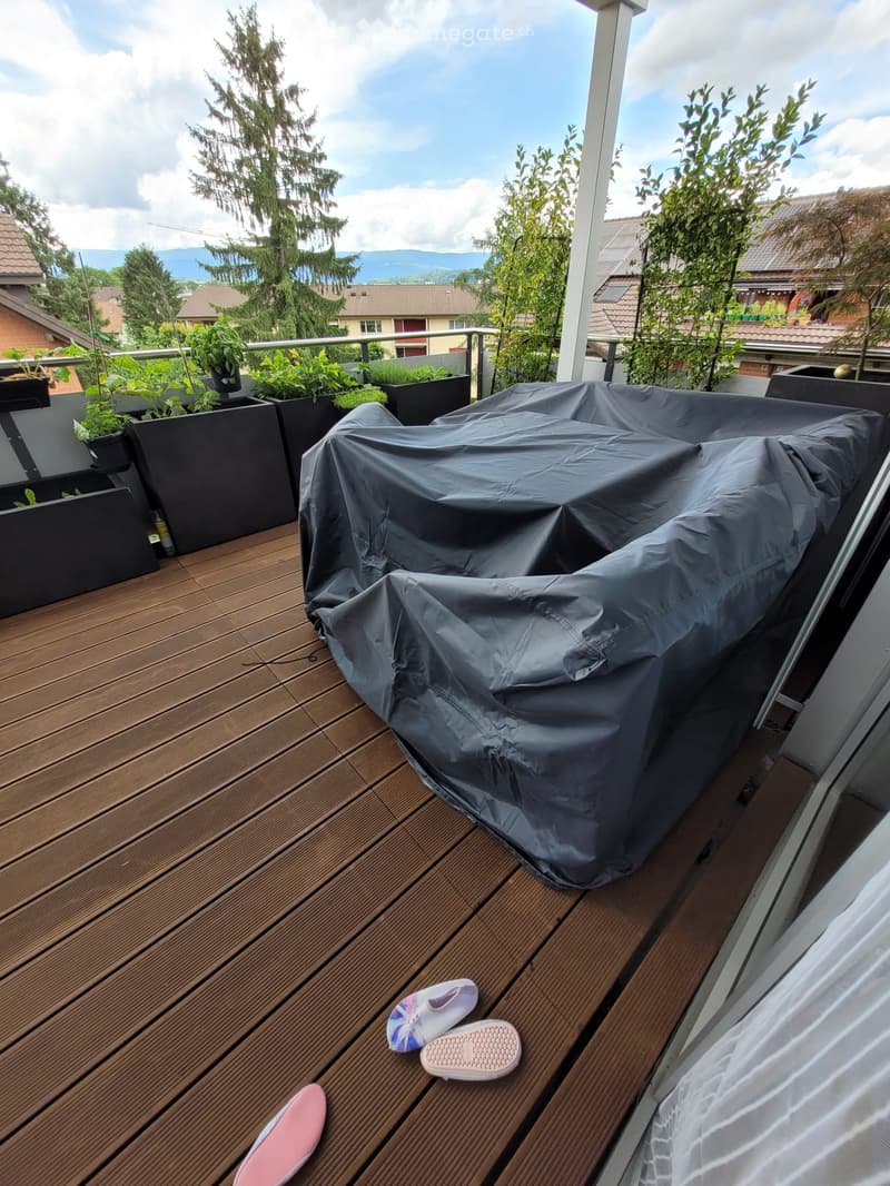 Wooden deck with covered furniture, potted plants, and a scenic view of the surrounding area.