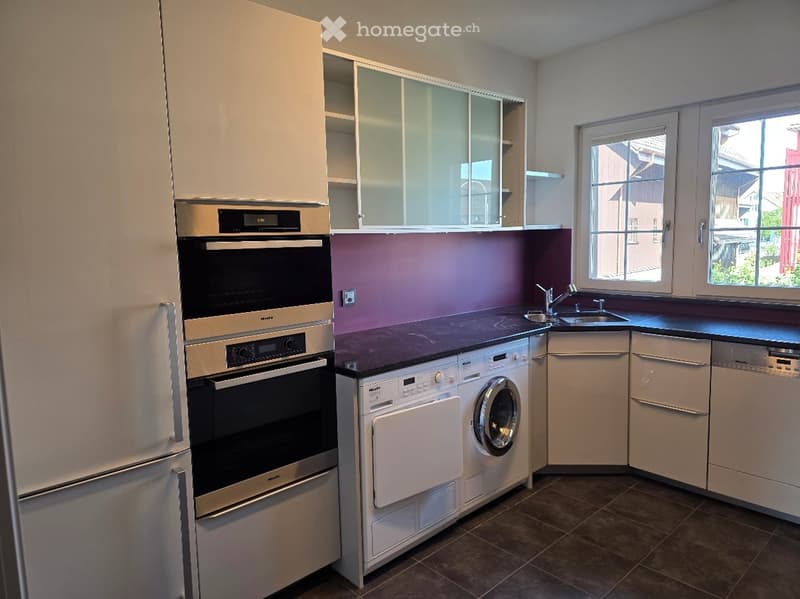 Modern kitchen with white cabinets, stainless steel appliances, and a dark countertop. Features include a refrigerator, oven, dishwasher, washing machine, and a sink with a faucet.