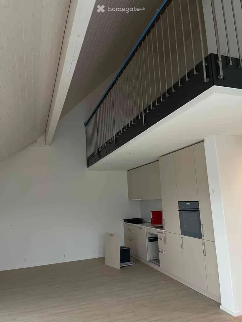 Empty room with light-colored cabinets, a staircase leading to an upper level, and a small kitchen area with a countertop and built-in appliances.