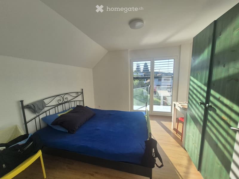 Bedroom with a blue bed, pillows, a small table, and a stool near the bed.