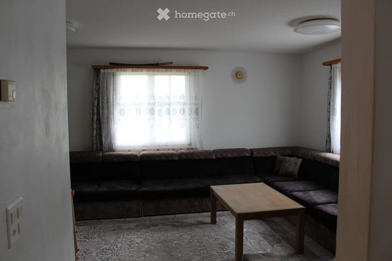 L-shaped sofa, wooden coffee table, white curtains, white walls, ceiling lamp, wall clock, power outlet