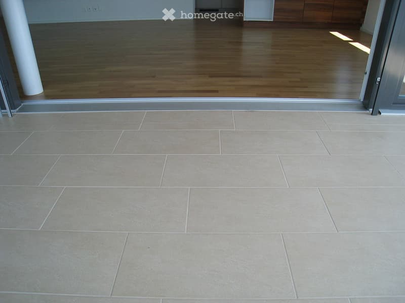 Empty room with wooden flooring and tiled area, no furniture or equipment visible.