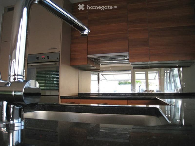 Modern kitchen with dark countertops, wooden cabinets, stainless steel faucet, and built-in oven.