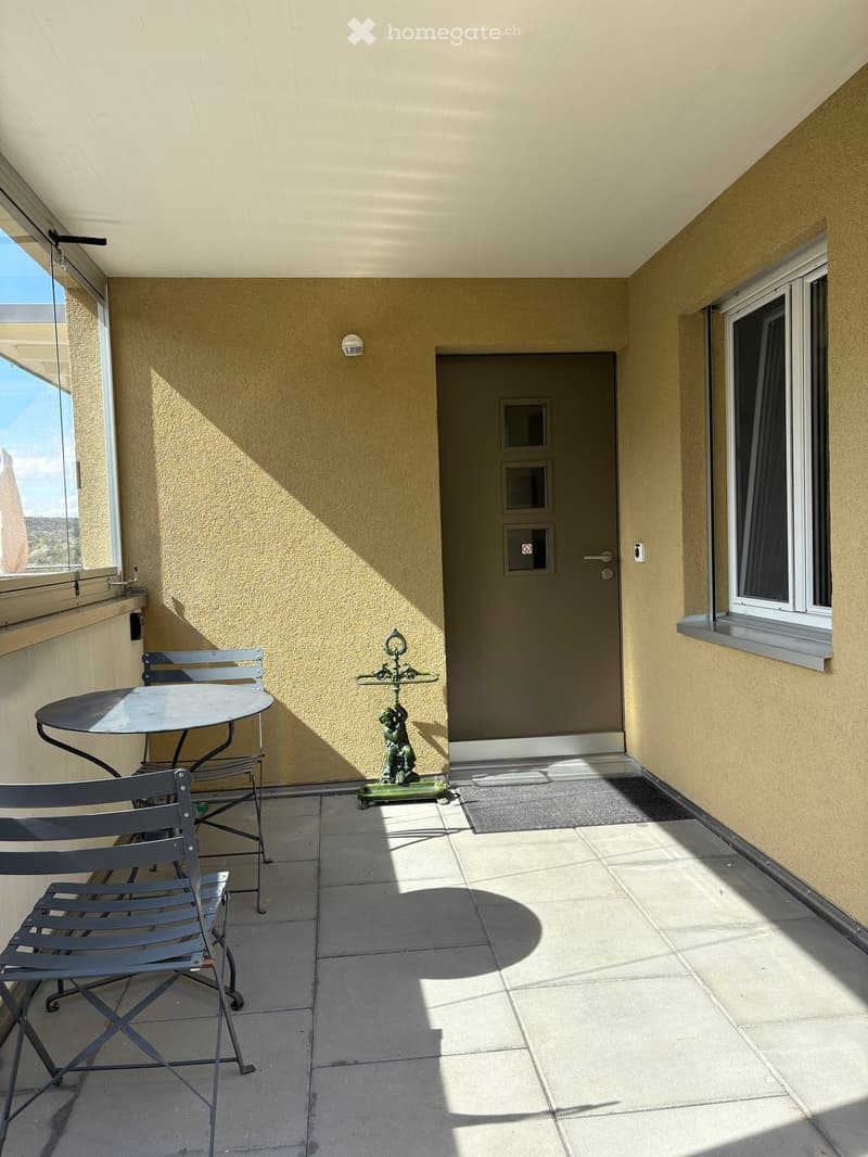 Balcony with tiled floor, beige walls, a round table with two chairs, and a decorative statue near the door.