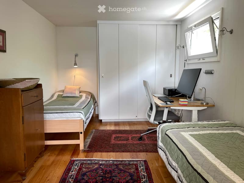 Cozy bedroom with two beds, a desk with a computer setup, a chair, a cabinet, and decorative items.