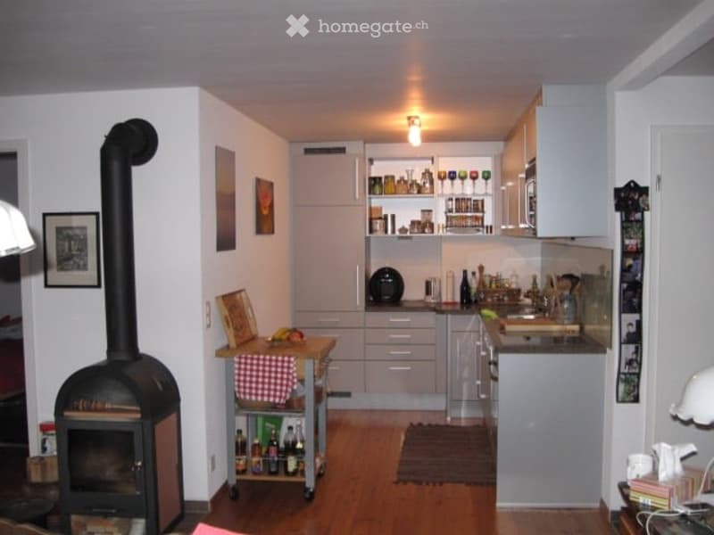 A modern kitchen with a fireplace, white cabinets, a kitchen counter, and a sink. There is a small table with a checkered tablecloth and a chair nearby.