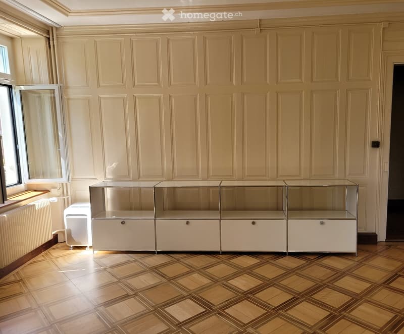 A room with wooden flooring, large cabinetry, and a radiator near the window.