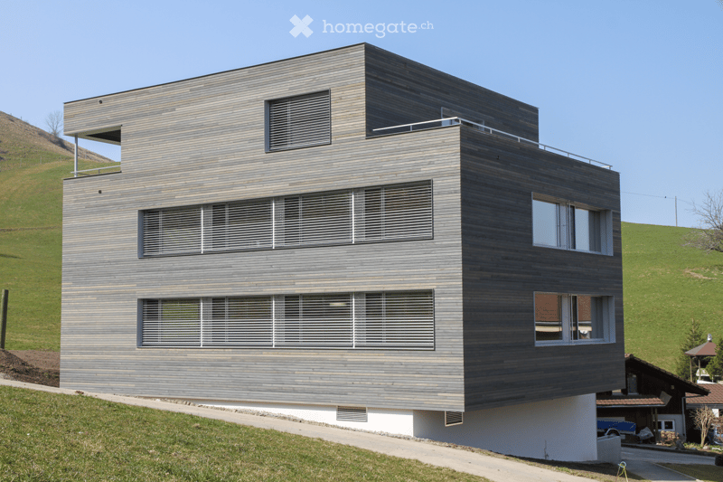 Modern architecture, wooden facade, multiple windows, balcony on top floor, white lower section, on a hill.