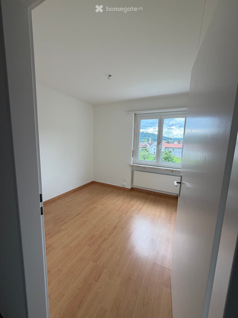 Empty room with wooden flooring, white walls, and a large window offering a view of the landscape.