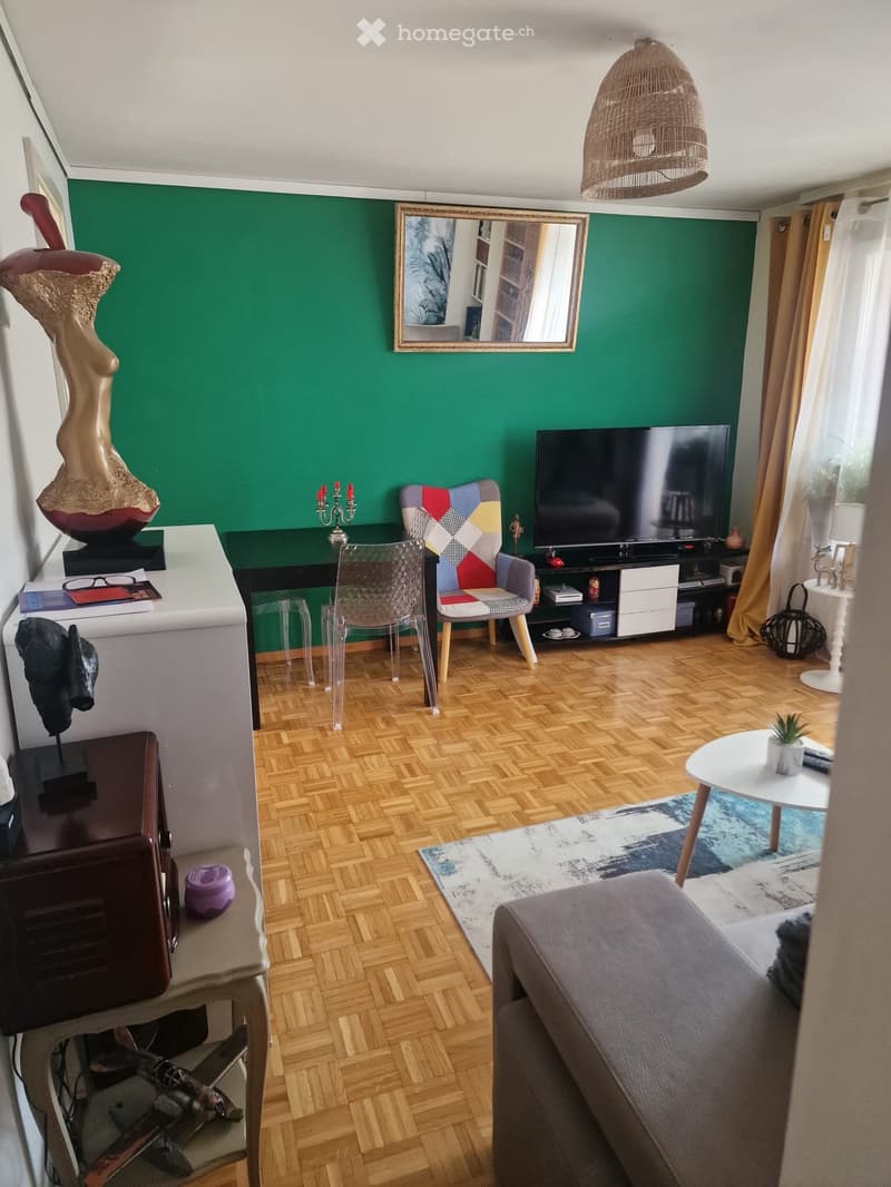Living room with wooden flooring, green accent wall, sofa, colorful chair, TV, mirror, and decorative items.