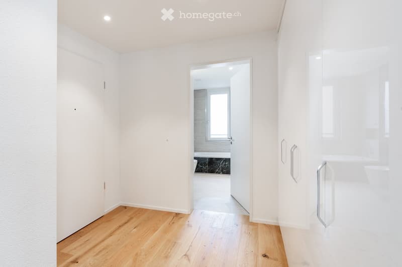 Bright, minimalist hallway with light wooden flooring, white walls, and a glass door leading to a modern bathroom with a bathtub and marble accents.