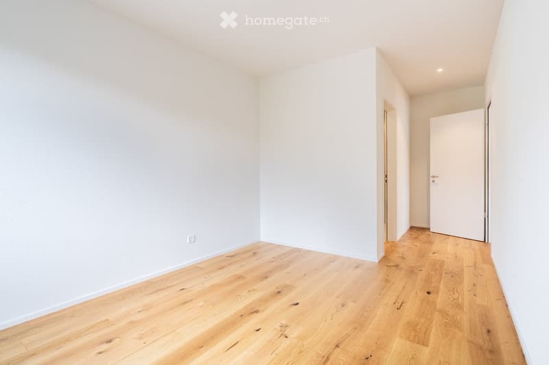 Empty room with light wooden flooring and white walls, featuring a closed door and a small recessed light fixture on the ceiling.