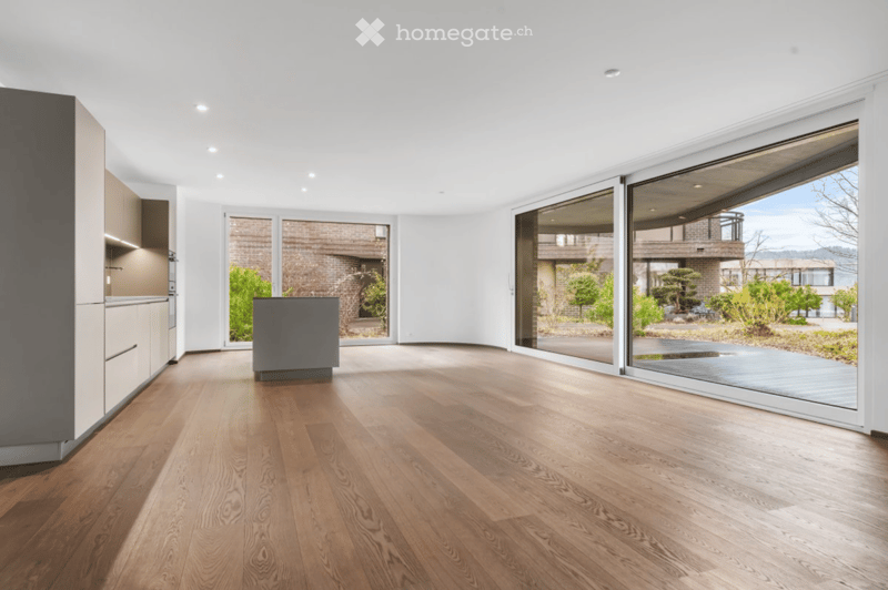 Bright, open-concept space with wooden flooring, large glass sliding doors, and a modern kitchen area visible on the left side.