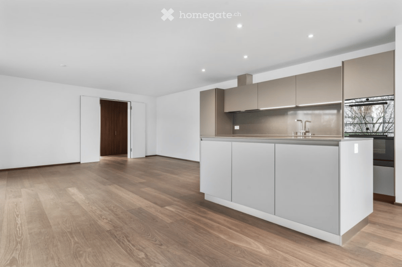 Modern kitchen with light grey cabinets, a central island, and a sleek faucet, featuring a wooden floor and white walls.