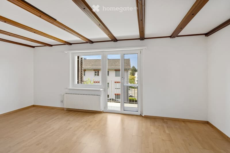Empty room with wooden flooring, white walls, large window, and sliding glass door leading to a balcony or outdoor area.