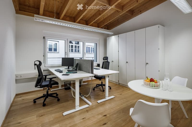 modern office room with two desks, two chairs, monitors, keyboards, and a round table with fruits
