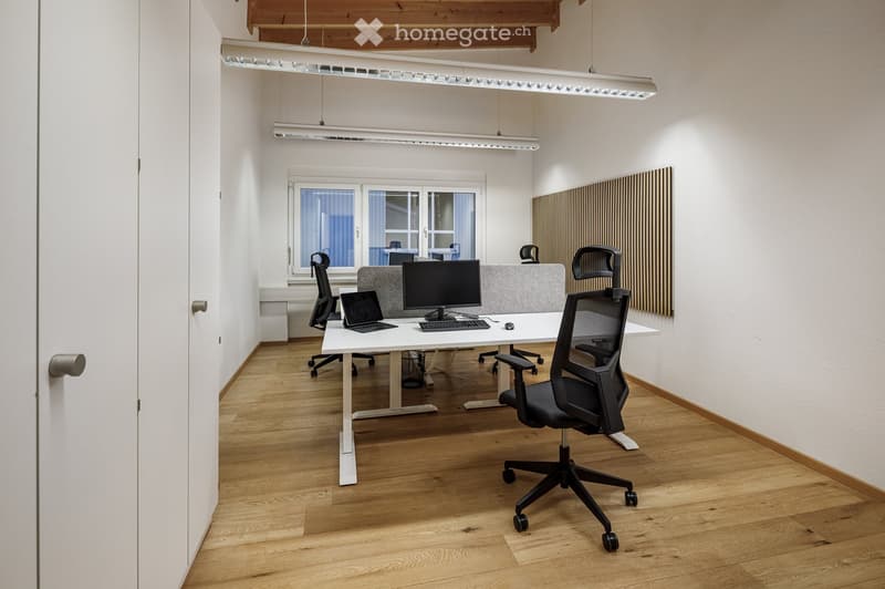 modern office room with white walls, wooden floor, white desk, black office chairs, monitors, keyboards, mouse, laptop, ceiling lights