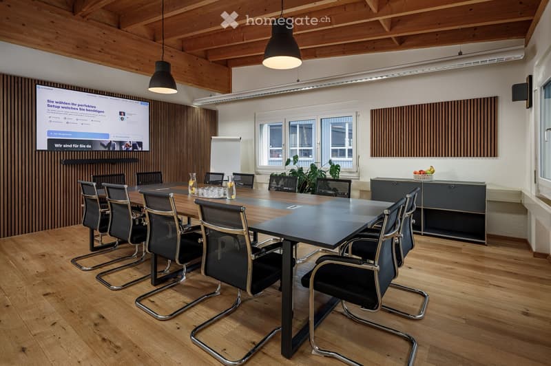 conference room with a large table, chairs, projector screen, wooden floor, wooden ceiling, windows, whiteboard, plant, and a cabinet with fruits