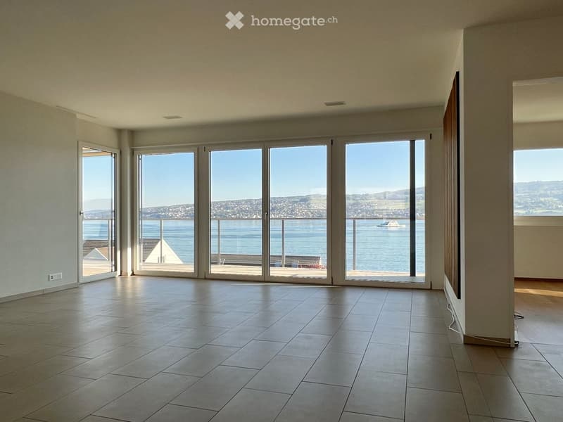 Empty room with large sliding glass doors leading to a balcony overlooking the ocean and cityscape.