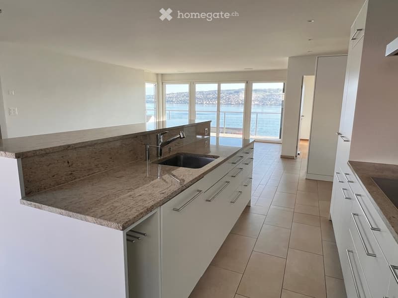 Modern kitchen with white cabinets, granite countertops, and a sink, overlooking a scenic waterfront view.