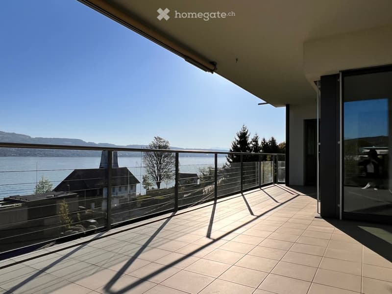 Balcony with tiled floor, glass railing, and scenic view of a lake and mountains.