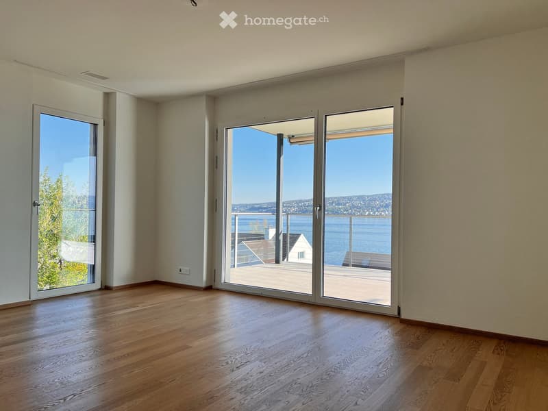 Empty room with wooden flooring, large sliding glass doors leading to a balcony with a scenic view of the water and distant landscape.
