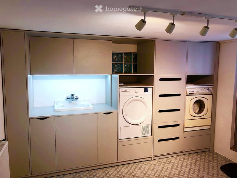 Modern, compact laundry room with built-in cabinets, a sink, and stacked washing and drying machines.