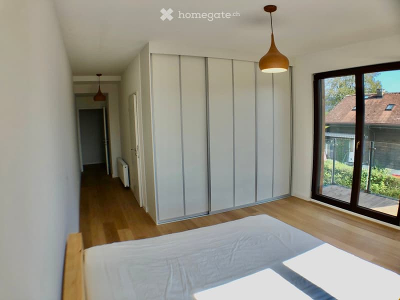 Bright bedroom with wooden flooring, a large bed, a sliding wardrobe, and a large window with a view of the garden.