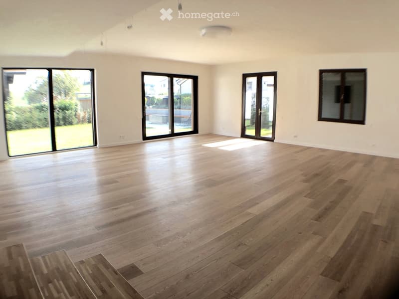 Empty room with light wooden flooring, large windows, and sliding doors leading to an outdoor area.