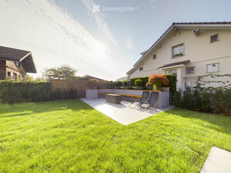 Well-maintained garden with a lawn, patio area, lounge chairs, and a small seating area near the house.
