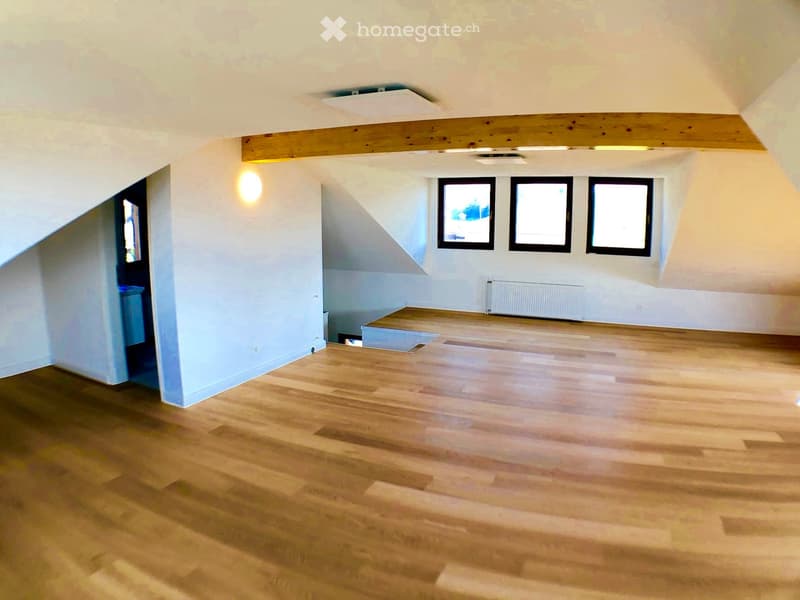 Empty room with wooden flooring, white walls, and three windows. The room has a slanted ceiling and a small radiator under the windows.