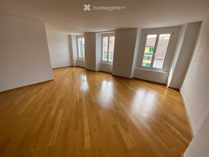 Empty room with wooden flooring and large windows, no furniture or equipment.