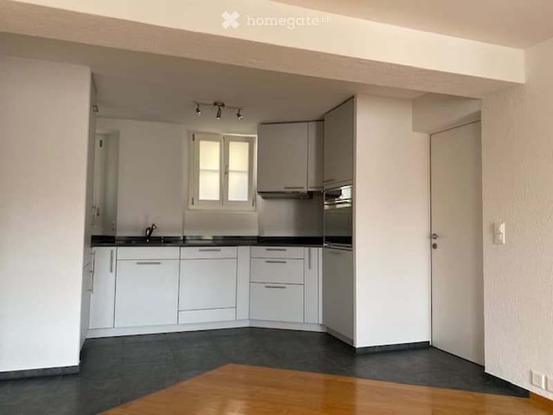 Modern kitchen with white cabinets, black countertops, and stainless steel appliances. Features a sink, faucet, and built-in oven. The space is well-lit with a ceiling light fixture.