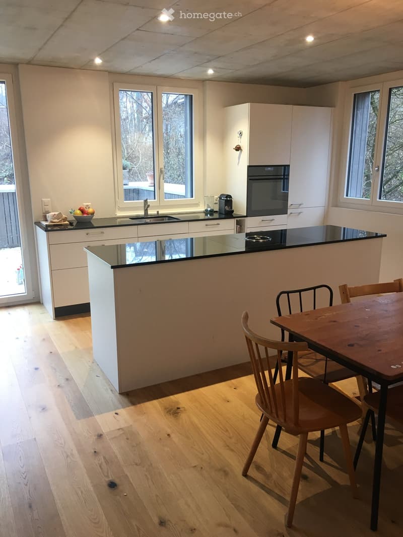 Modern kitchen with white cabinets, black countertops, a central island, and a dining area with a wooden table and chairs.
