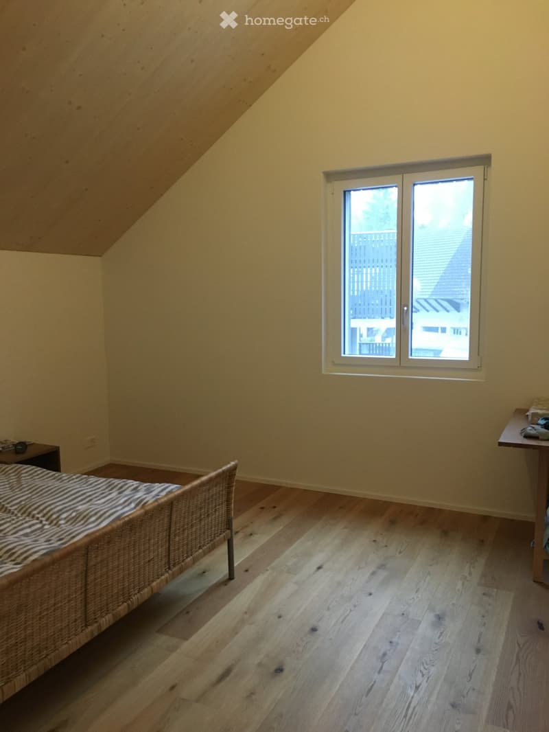 Bright bedroom with wooden flooring, a wicker bed frame with striped bedding, a small table, and a window with a view of the outside.