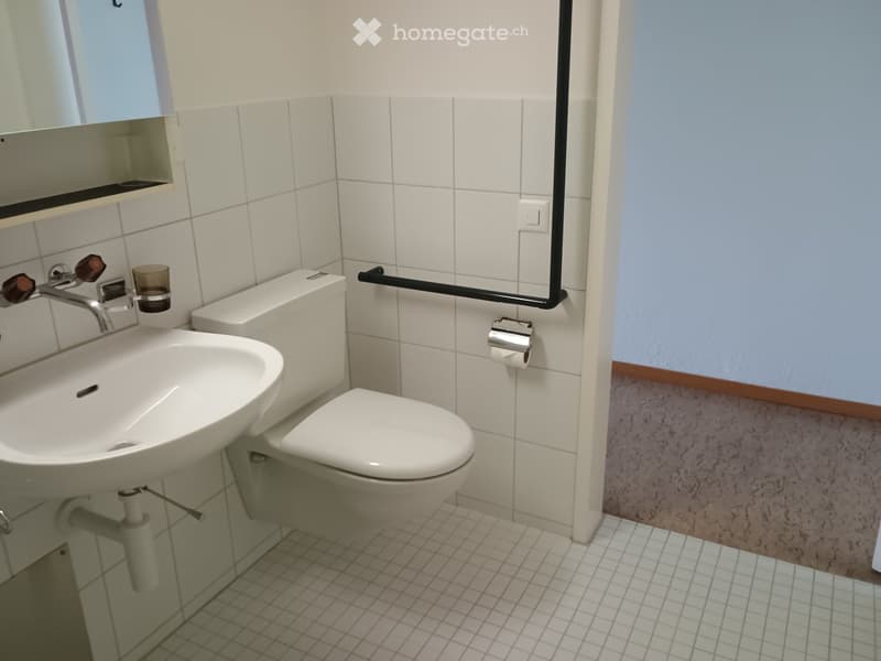 Modern bathroom with white tiles, a sink, a toilet, a mirror, and a cup on the sink counter.
